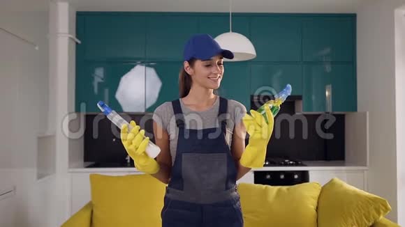 美丽的年轻女子穿着工作服两瓶洗涤剂混在一起站在舒适的厨房里视频的预览图