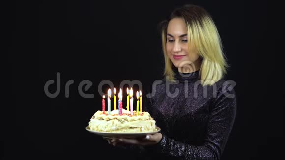 女孩拿着一个带蜡烛的节日蛋糕一个年轻的女人站在一件闪亮的晚礼服上孤立的黑色视频的预览图