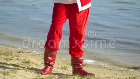 圣诞老人拿着一袋礼物站在河边或湖边圣诞老人把一个带礼物的袋子放在沙子上一种视频的预览图