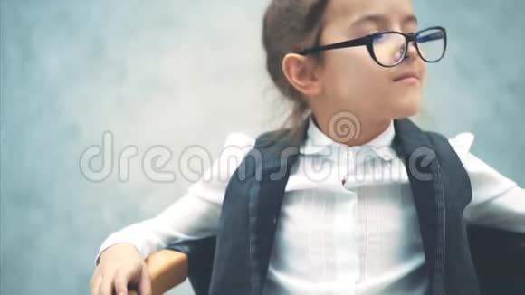灰色背景的小商业女孩在这悲伤的坐在椅子上把手放在手臂上戴眼镜视频的预览图