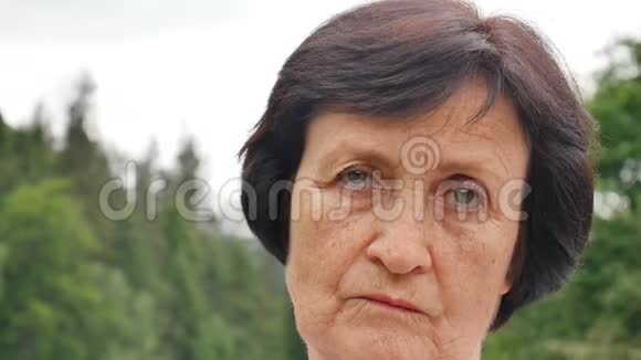 悲伤的成熟女士一头乌黑的短发脸上布满皱纹正看着山岗上的摄像机她的脸上带着绿色视频的预览图