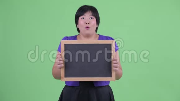 快乐的年轻超重的亚洲女人拿着黑板看上去很惊讶视频的预览图