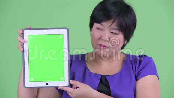 一位年轻体重超重的亚洲女性一边讲着数字平板电脑视频的预览图