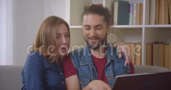 年轻自信的白种人夫妇坐在沙发上用笔记本电脑在家里专心地讨论视频的预览图