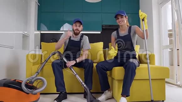 微笑着年轻的男女清洁服务团队坐在厨房的沙发上竖起大拇指的手势视频的预览图