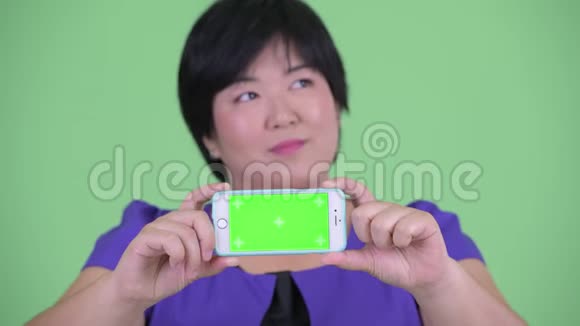 快乐年轻超重的亚洲女人的脸思考和显示电话视频的预览图