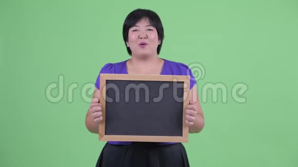 快乐年轻体重超重的亚洲女人拿着黑板说话视频的预览图