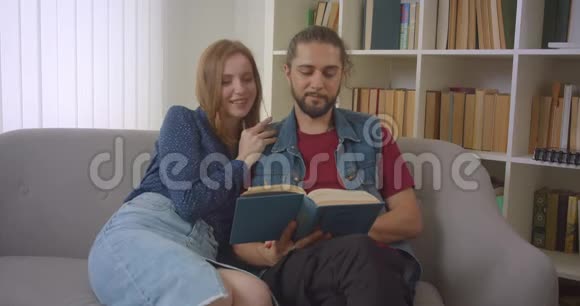 这对年轻的白种人夫妇坐在沙发上看书在家里很感兴趣也很积极视频的预览图