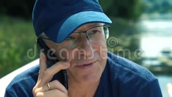 一个穿着蓝色帽子t恤和眼镜的头发花白的男人坐在一个房间里一边打电话一边笑视频的预览图