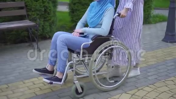 年轻的穆斯林残疾人戴着传统的围巾戴着轮椅的眼镜在街上与穆斯林朋友交谈视频的预览图