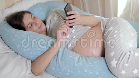 孕妇用智能手机和触摸式枕头躺在床上视频的预览图
