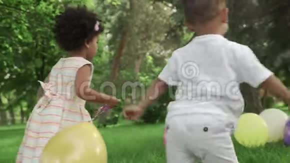 小非裔美国女孩和男孩在公园里玩五颜六色的气球视频的预览图