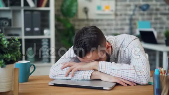 年轻男性员工睡在办公桌上在工作中放松的肖像视频的预览图
