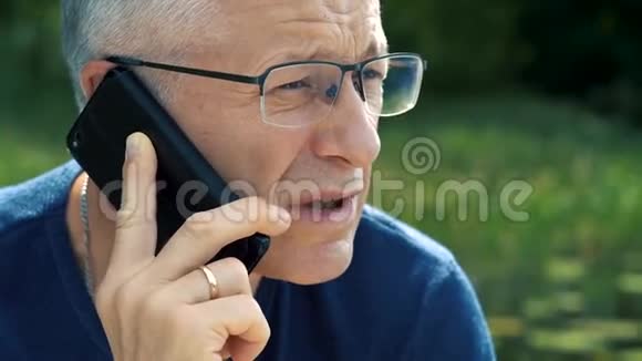 一个穿着蓝色t恤和眼镜头发花白严肃认真的男人坐在船上严格地打电话视频的预览图