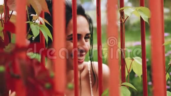 一个令人惊叹的漂亮女孩站在花园篱笆前看着前方冷静的眼神和笑容视频的预览图