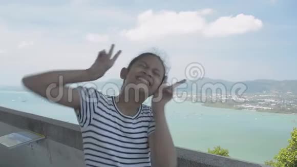 亚洲可爱的女孩穿着休闲装在观景塔上用滑稽的姿势拍照风景迷人视频的预览图