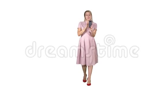 微笑的女人穿着粉红色的裙子在白色的背景上做视频呼叫和行走视频的预览图