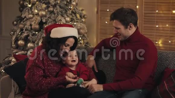 一个快乐可爱的年轻家庭和一个微笑的小男孩坐在靠近圣诞树的客厅里的沙发上视频的预览图