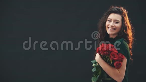 美丽的卷发黑发女孩站着享受着红色玫瑰的花束微笑着视频的预览图