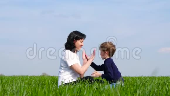 妈妈和小朋友坐在绿草上玩耍互相拍打的手家庭幸福关爱的理念视频的预览图