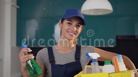 30多岁的女孩穿着清洁衣服在蓝黑厨房的背景上喷洒绿色洗涤剂视频的预览图