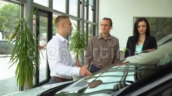 一家汽车经销商的顾问为几个买家介绍一辆车异性夫妻买车视频的预览图