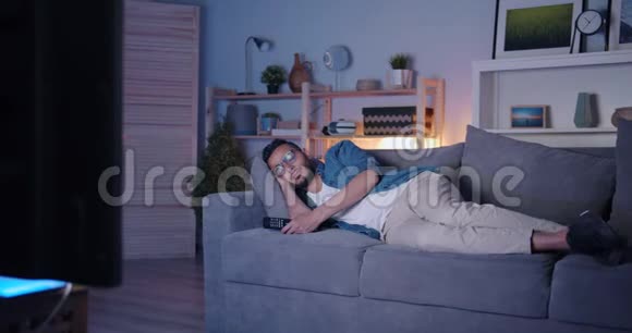 阿拉伯男人睡在电视前的沙发上晚上在黑暗的平板上放松视频的预览图