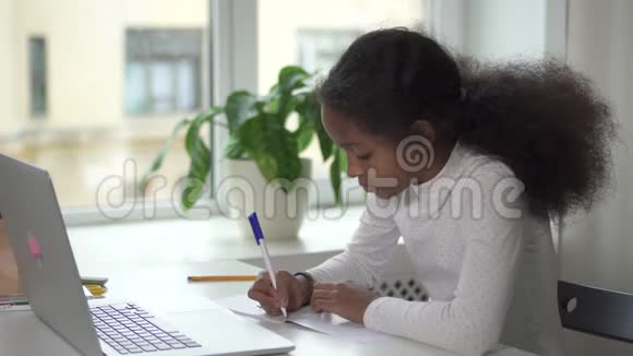 年轻漂亮的女孩坐在桌子旁用新的现代数字技术笔记本电脑做作业视频的预览图
