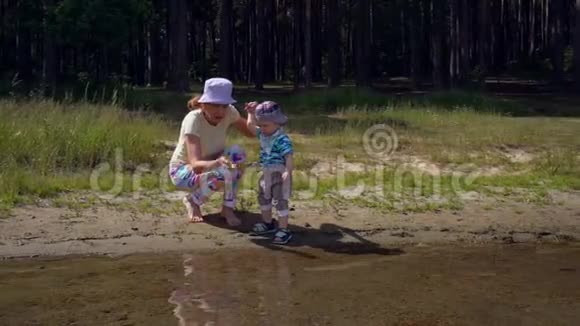 妈妈和她的小儿子在一个森林湖的岸边玩小石子视频的预览图