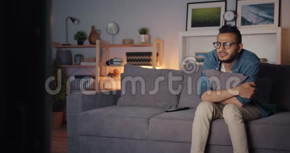 悲伤的阿拉伯男人看着电视哭着擦着眼睛独自坐在沙发上视频的预览图