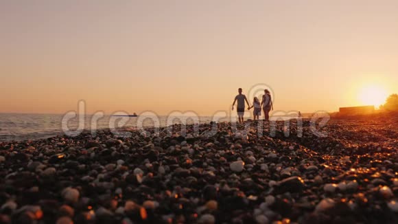 一家人带着一个孩子在海边夕阳下散步在度假胜地一起放松视频的预览图