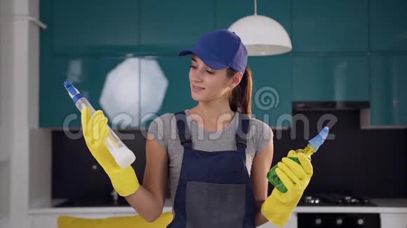 年轻的微笑妇女从清洁服务比较两个喷雾清洁剂在她的手中的菜肴视频的预览图