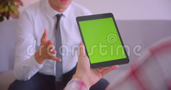 客户服务经理与客户手持平板电脑的特写肖像办公室里有绿色的关键屏幕视频的预览图