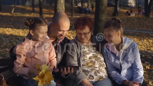 有着成年儿子和女儿的女人坐在公园的长凳上在智能手机上看照片链接视频的预览图