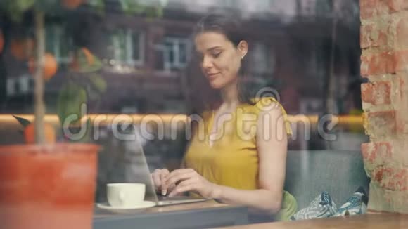 微笑的女孩在咖啡馆里用手提电脑打字专注于活动视频的预览图