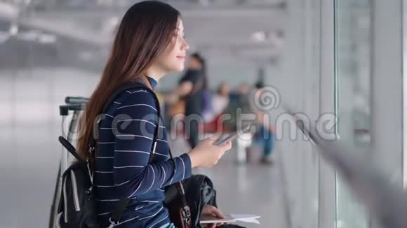 年轻的女旅客在机场等候时使用智能手机视频的预览图