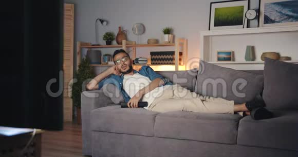 疲惫的非裔美国人晚上看电视独自躺在沙发上打哈欠视频的预览图