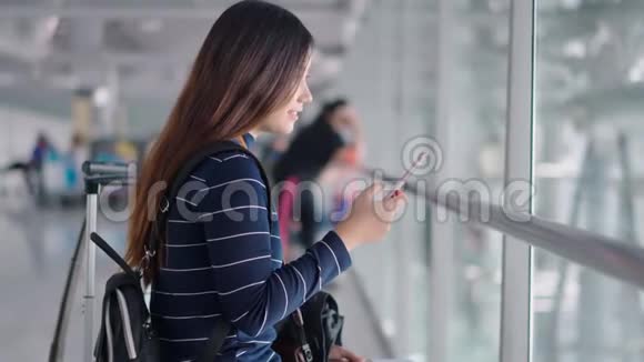 年轻的女旅客在机场等候时使用智能手机视频的预览图