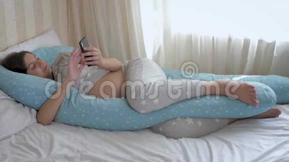 孕妇用智能手机和胃躺在床上视频的预览图