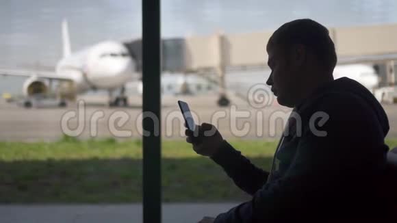 美国男商人在机场用手机看手机应用程序视频的预览图