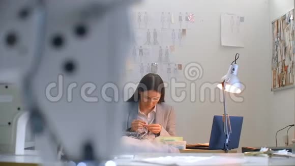 一位年轻的女设计师在工作室里缝一件连衣裙做衣服缝纫珠子和珠宝裁缝装饰视频的预览图