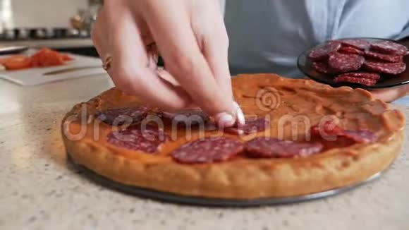 女孩把香肠放在厨房的自制披萨上视频的预览图