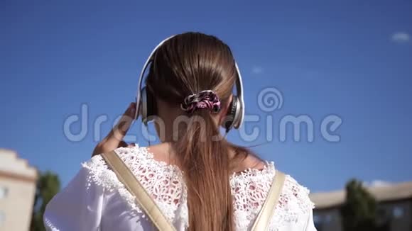 年轻女孩在城里旅行沿街散步的女游客戴耳机的女孩背着背包视频的预览图