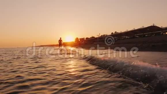 日落时一个少年绕着冲浪线奔跑的剪影视频的预览图