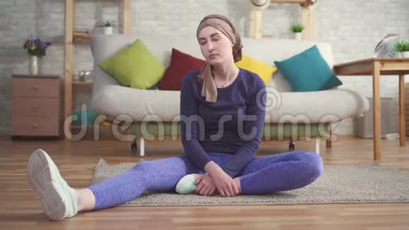 年轻女性癌症患者化疗后戴头巾在家训练前做伸展运动视频的预览图