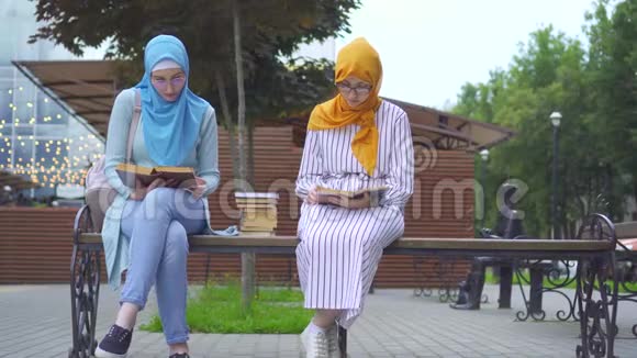 两名戴着传统围巾手里拿着书的穆斯林学生坐在长凳上看书视频的预览图