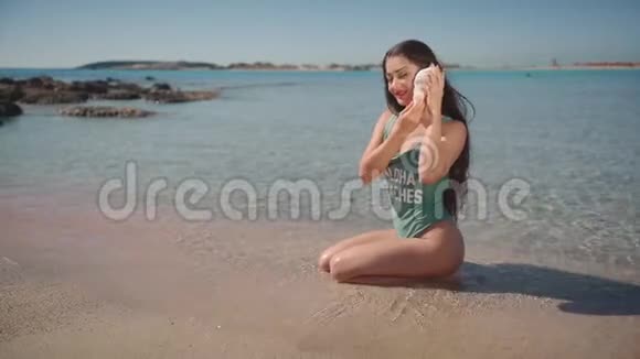 穿着泳衣在海边听贝壳的漂亮女人水疗旅游奢侈生活方式博客美容理念视频的预览图