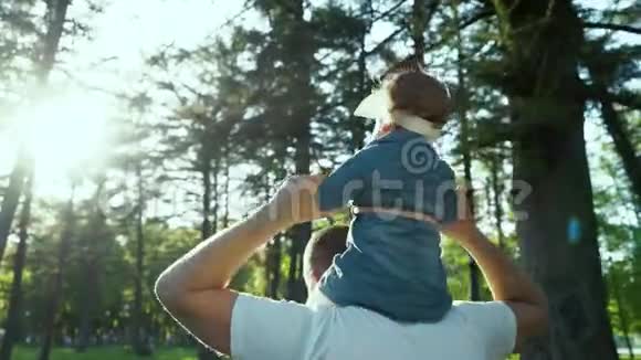 在公园镜头耀斑中父亲和他的小女孩肩上玩耍的后景视频的预览图