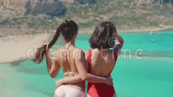 两个穿着泳衣的漂亮女孩举手欣赏蓝色泻湖的景色完美的现实旅游博客生活方式视频的预览图