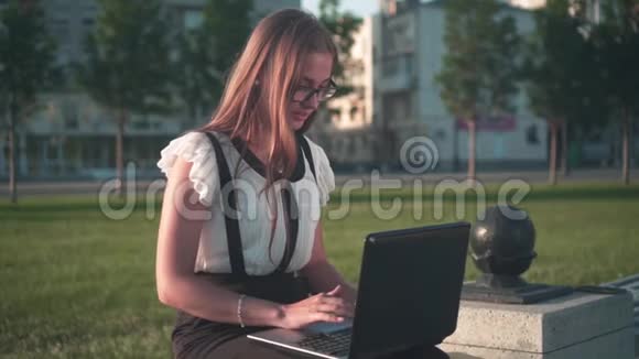 商务女性穿着白色衬衫和眼镜坐在长凳上在笔记本电脑上工作这个女孩对工作不满意生气视频的预览图